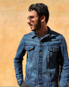Kille iklädd jeansjacka, står i profil mot en gulvägg