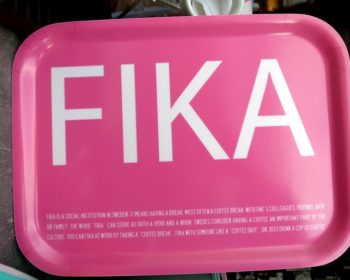 En rosa bricka som det står fika på samt en förklarande text på engelska om vad fika är.